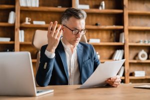 Man staring at papers with hand raised while sitting at his desk