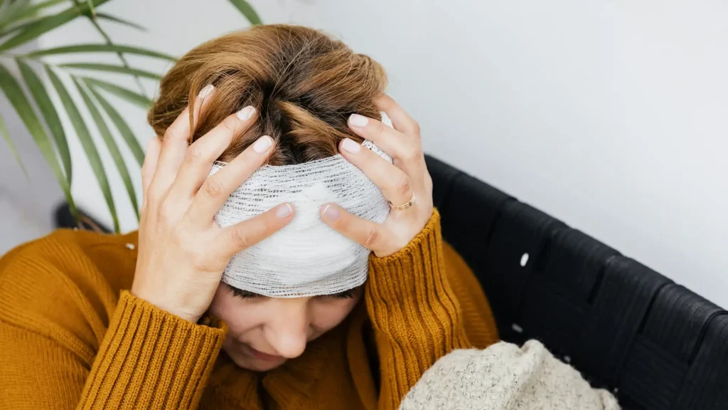 Injured woman holding her head with a bandage wrapped around her forehead.