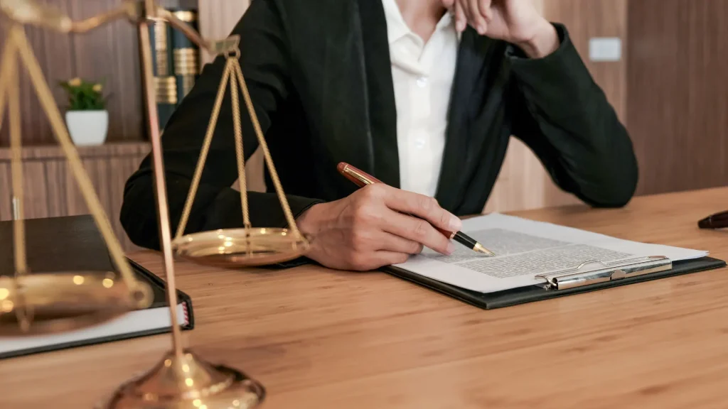 A lawyer is reviewing legal documents while holding a pen, with a scale of justice placed next to them.