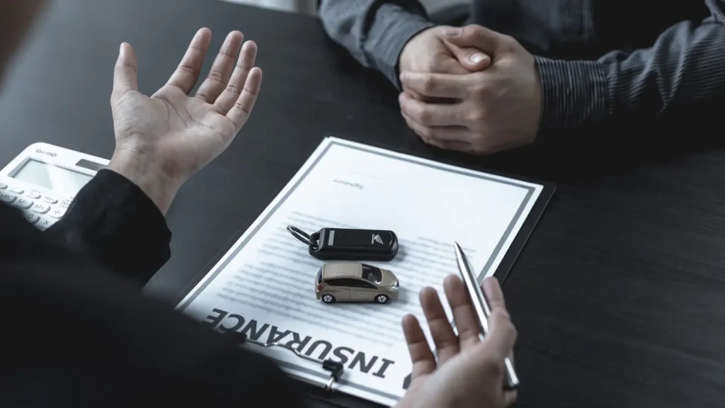 Two people discussing insurance, with a document and car keys on the table