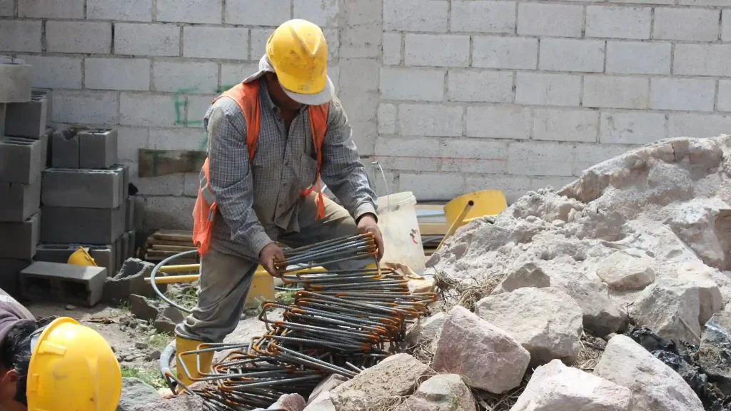 Construction worker wearing a hard hat and safety gear, handling metal rods at a construction site
