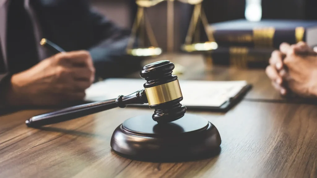 A gavel resting on a wooden desk with scales of justice in the background