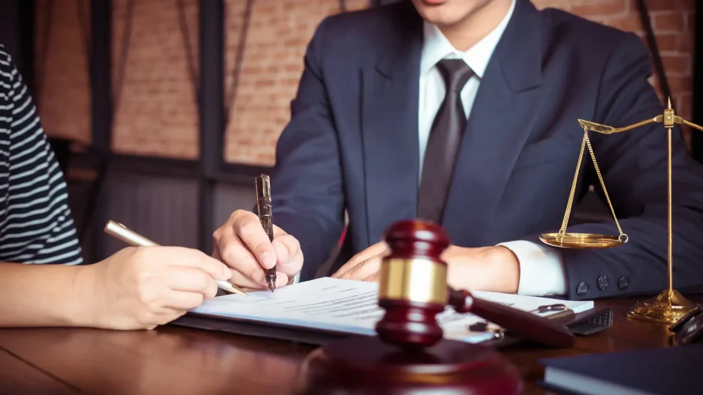 Two individuals in formal attire signing legal documents, with a gavel in the foreground, symbolizing a legal agreement.