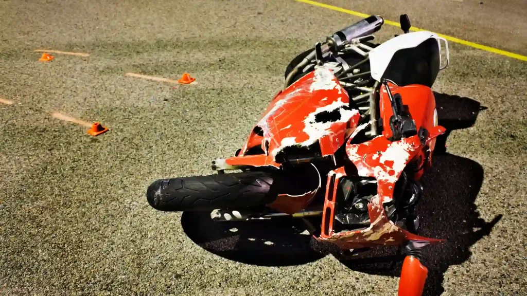 Close-up of a red motorcycle with severe damage on the road after an accident, with parts scattered nearby