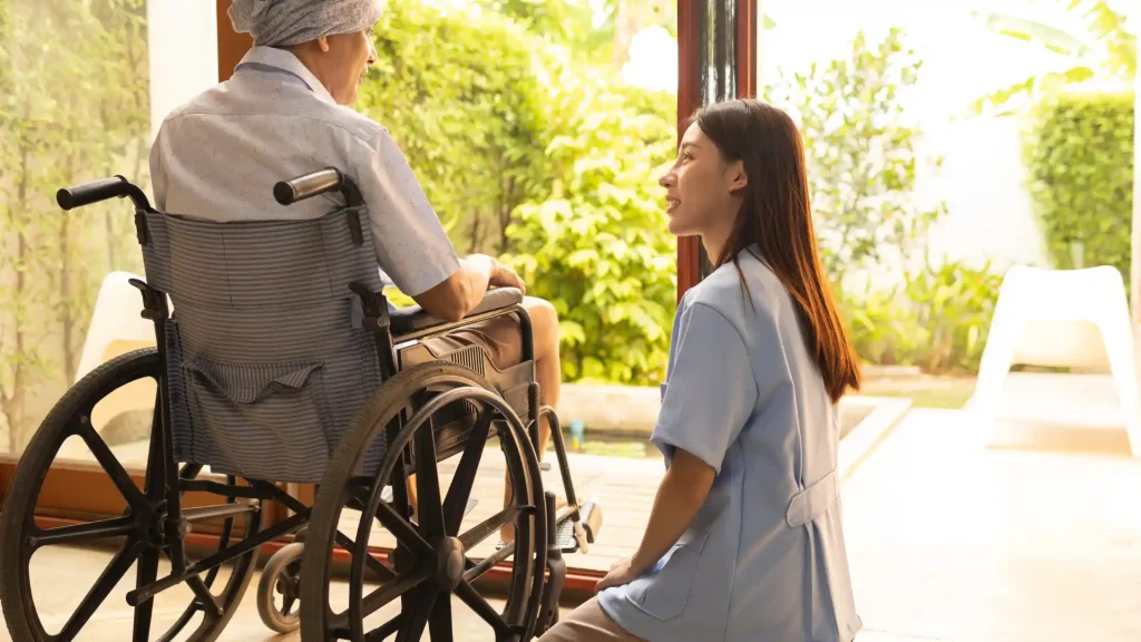 A caregiver speaking with an elderly patient in a wheelchair, providing compassionate support in a bright and peaceful setting
