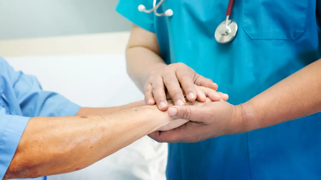 A healthcare professional holding a patient's hand gently in a hospital setting
