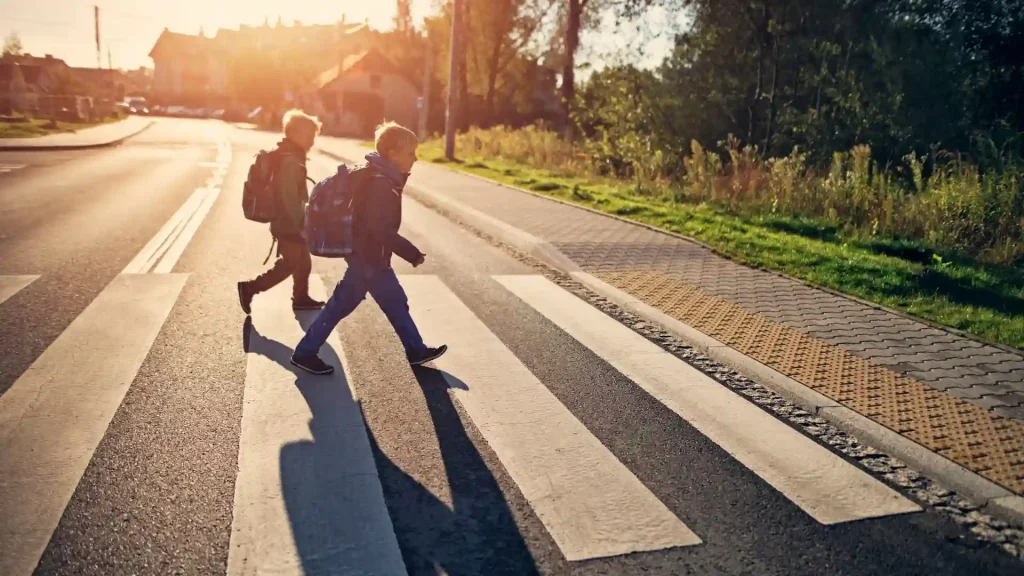 Two people crossing a pedestrian crosswalk during sunset.