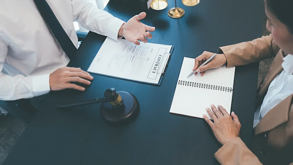 Gavel, legal file, and scales on table as lawyer explains paperwork to client taking notes