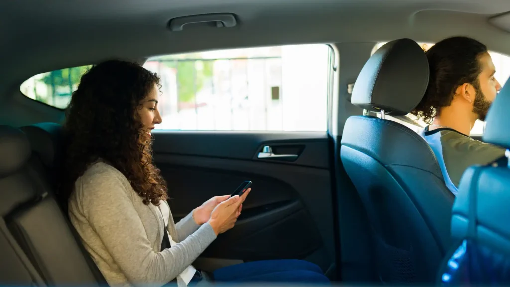 Smiling woman sitting in the back seat of a car, looking at her phone