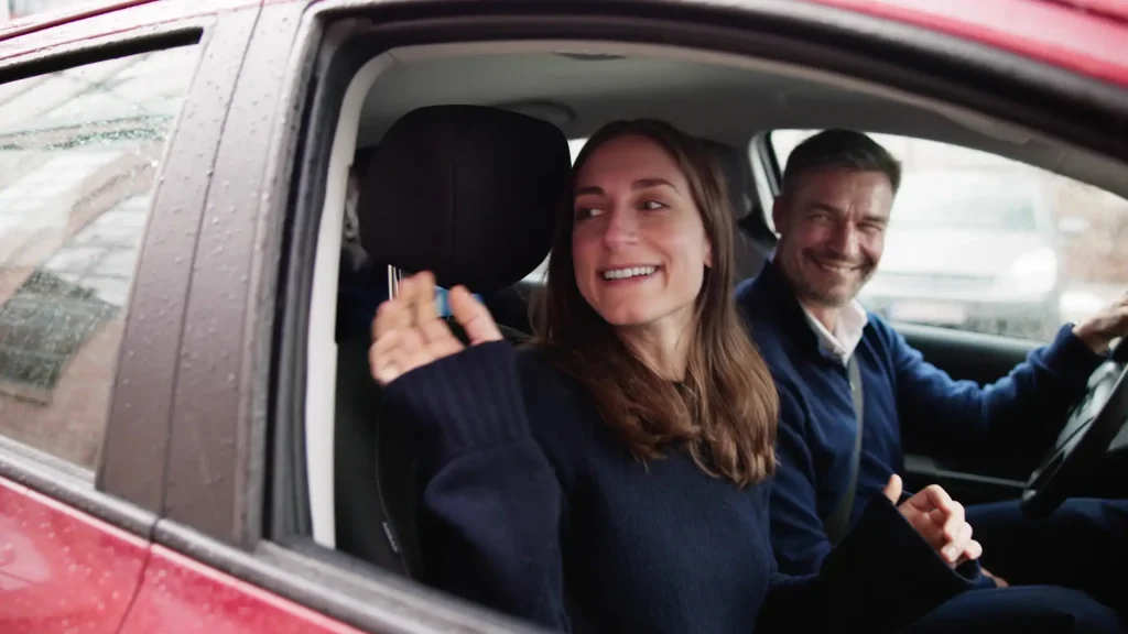 Smiling woman waving from a car window with man driving.