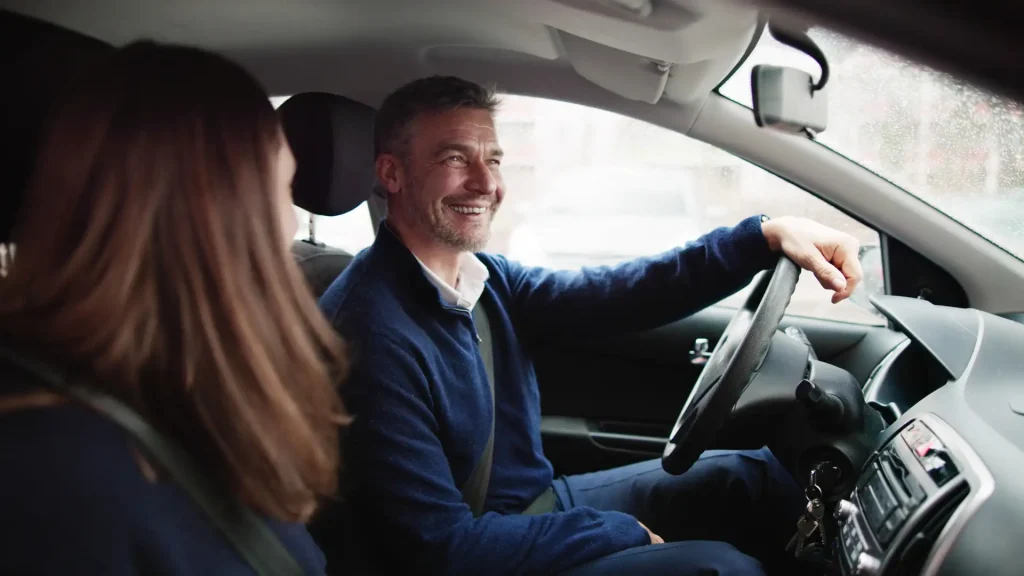 Smiling man driving a car with a passenger.