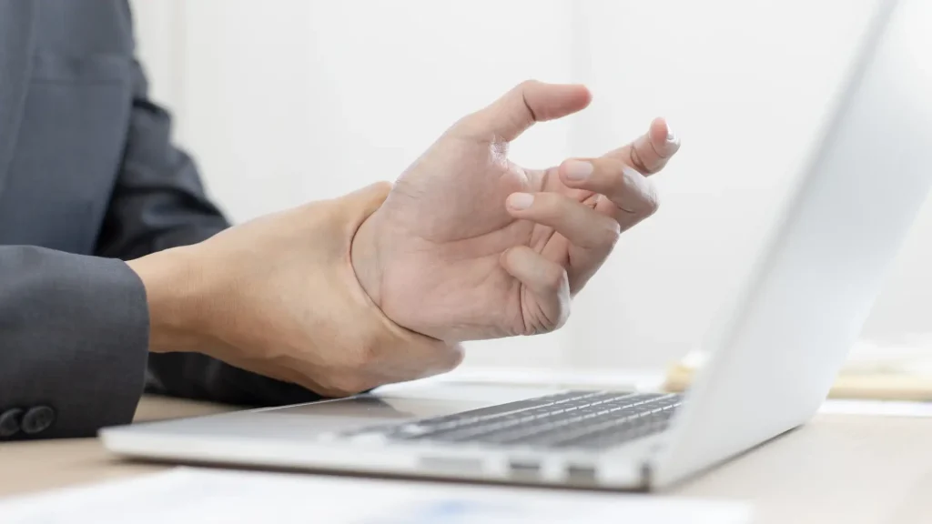 Close-up of an injured hand resting on a laptop keyboard, with a visible bandage on the wrist