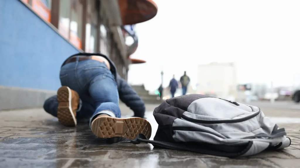 Person who has tripped and fallen on the sidewalk, with their backpack nearby