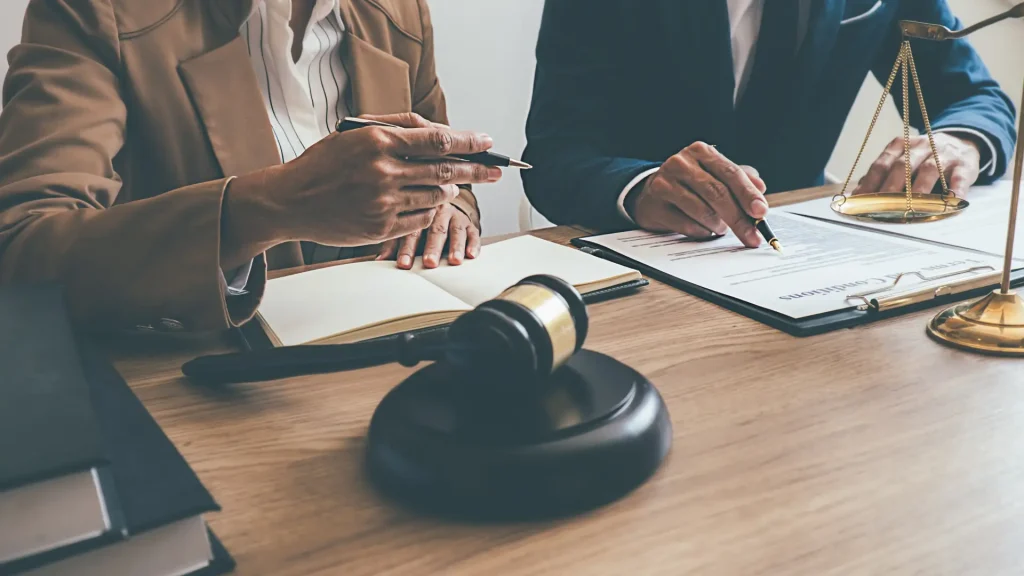 A close-up of two people sitting at a table discussing legal documents, with a gavel in the foreground.