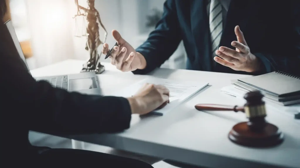 Two professionals discussing legal documents at a desk, with a small statue of Lady Justice in the background, symbolizing legal consultation