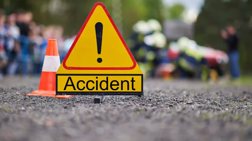 A yellow accident warning sign on the road with emergency responders in the background at the scene of an accident