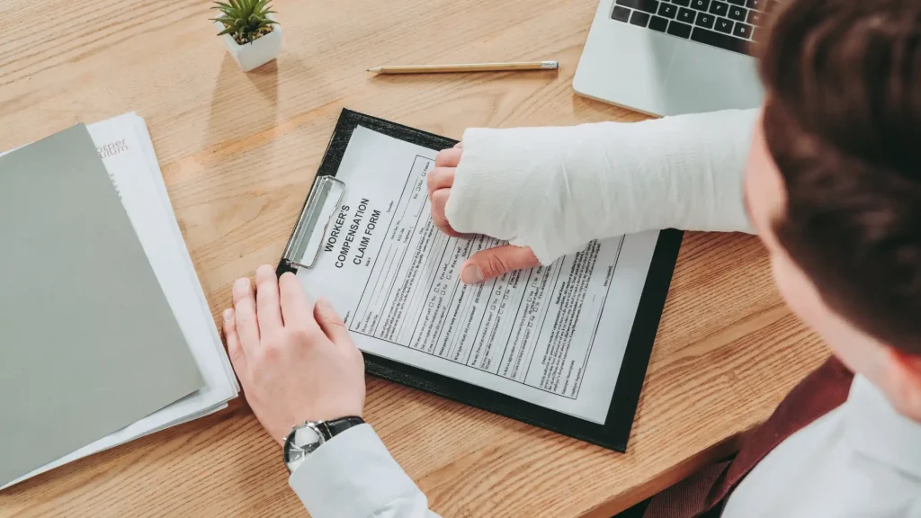 Person with arm cast filling out a compensation claim form on a clipboard.