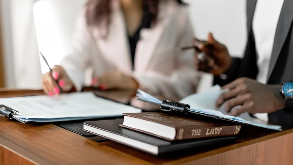 Two people discussing legal documents with law books on the desk.