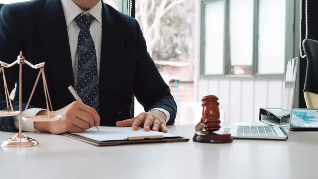 A lawyer in a suit signing legal documents with a gavel placed on the table, signifying legal proceedings