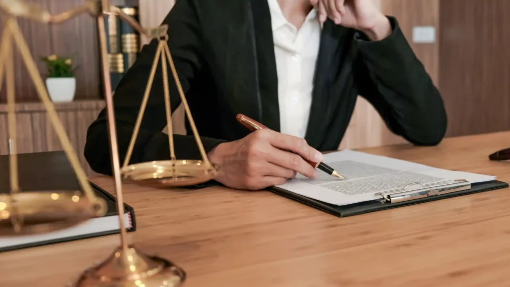 A lawyer reviewing documents and writing notes next to a golden scale of justice