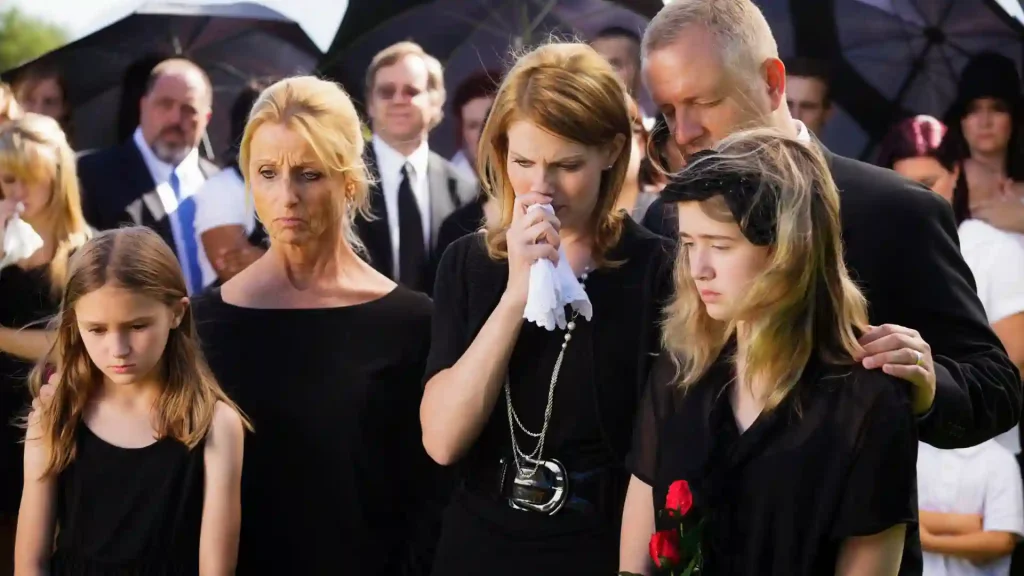 Mourners at a funeral, expressing grief and loss, with some holding tissues and others in quiet reflection