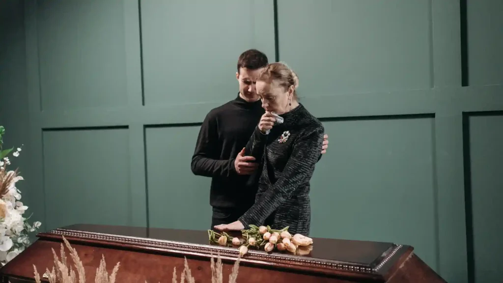 Grieving couple standing by a coffin, holding each other for support.